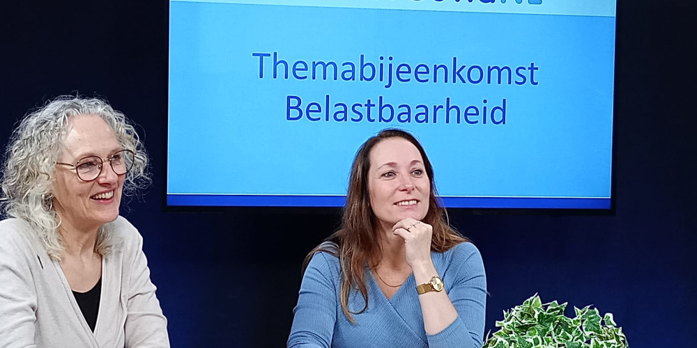Margriet links en spreker Nicole rechts aan tafel voor een scherm waar de presentatie zichtbaar op is